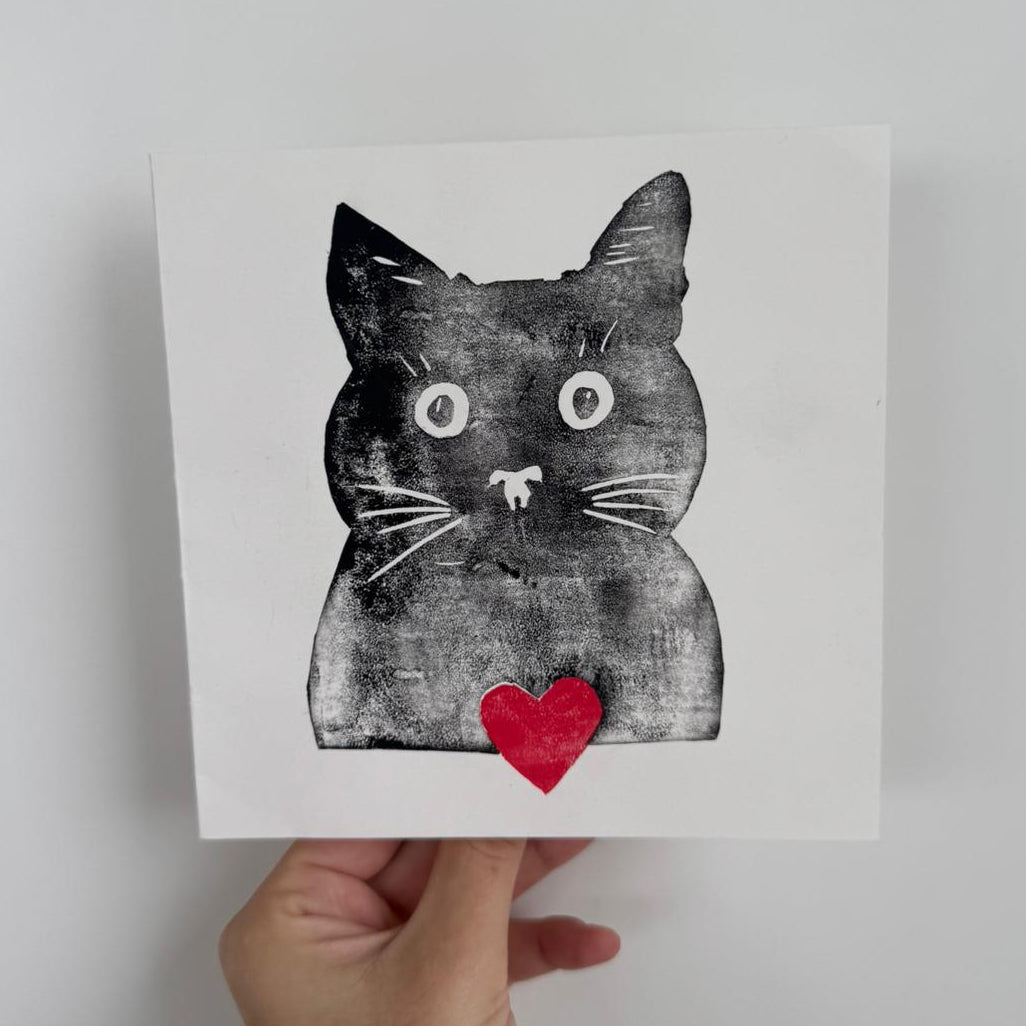 Handgemachte Linoldruckkarte mit schwarzer Katze und rotem Herz auf weissem Hintergrund. Minimalistisches, verspieltes Motiv – ideal als Grusskarte, Valentinskarte oder Geschenk für Katzenliebhaber.